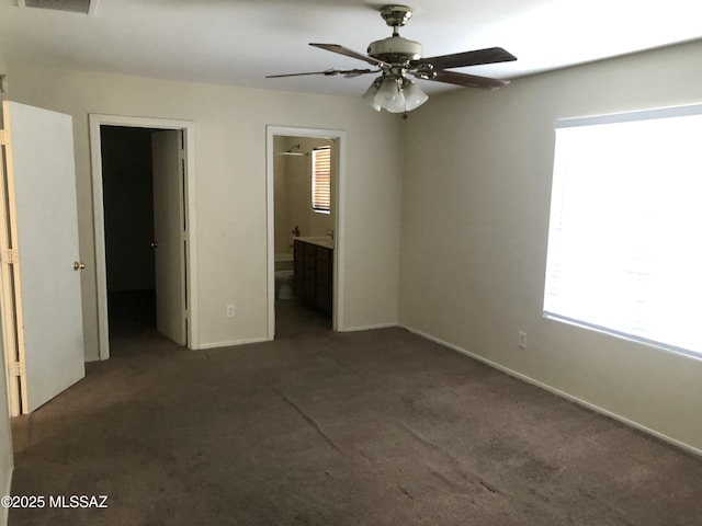 unfurnished bedroom with carpet floors, a walk in closet, ensuite bathroom, a ceiling fan, and baseboards