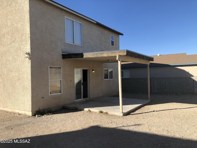 rear view of house with stucco siding, fence, and a patio