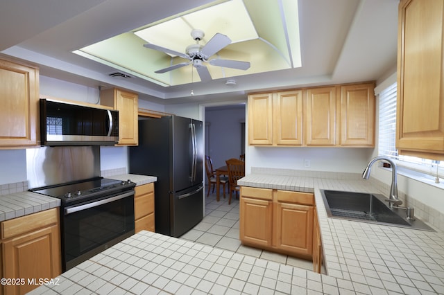 kitchen with a tray ceiling, tile countertops, stainless steel microwave, freestanding refrigerator, and black range with electric cooktop