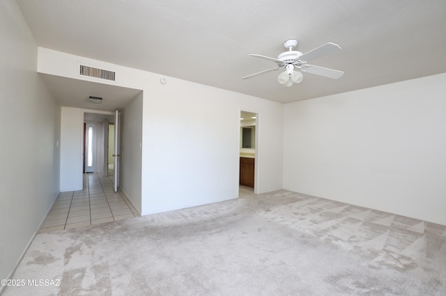 spare room with light colored carpet, visible vents, ceiling fan, and light tile patterned floors