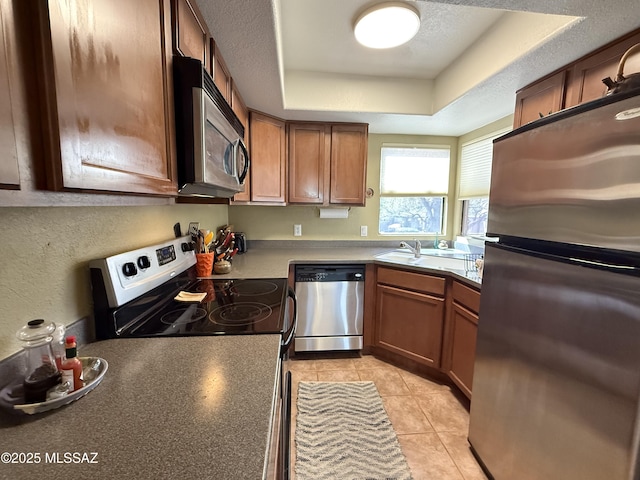 kitchen with light tile patterned floors, stainless steel appliances, a raised ceiling, a textured wall, and a textured ceiling