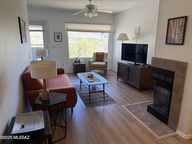 living room featuring a ceiling fan, a fireplace, baseboards, and wood finished floors