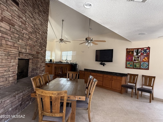 dining room with light tile patterned floors, a large fireplace, ceiling fan, a textured ceiling, and high vaulted ceiling