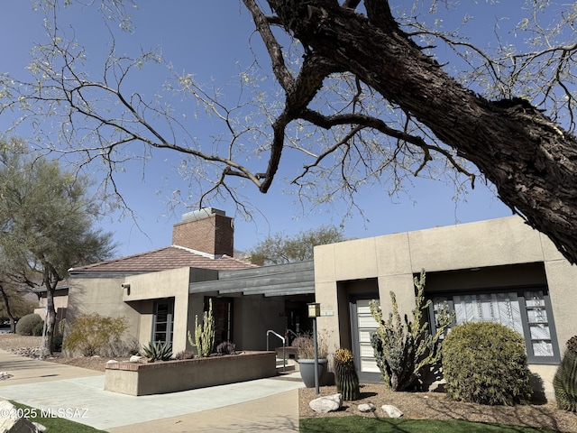 rear view of property with a chimney and stucco siding