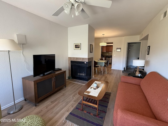 living area featuring ceiling fan, light wood finished floors, a fireplace, and visible vents