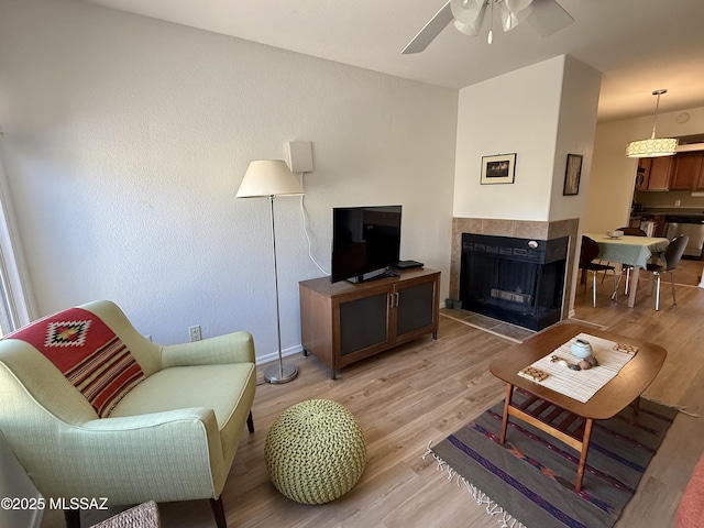 living room with light wood-type flooring, ceiling fan, and a fireplace