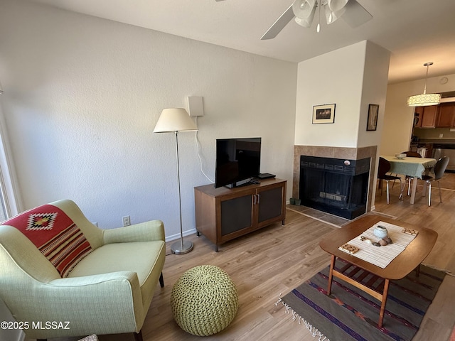 living room with a ceiling fan, a fireplace, and light wood-style flooring