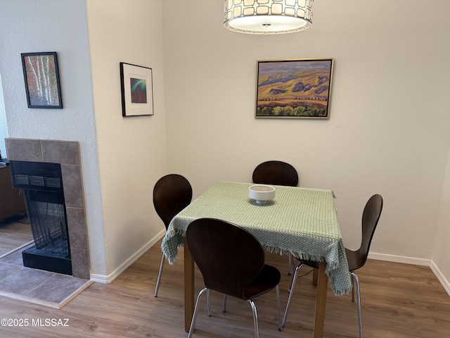 dining room featuring a tiled fireplace, baseboards, and wood finished floors