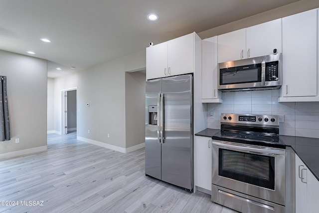 kitchen featuring dark countertops, tasteful backsplash, light wood finished floors, appliances with stainless steel finishes, and white cabinets