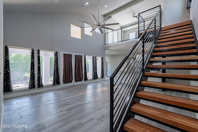 stairs featuring a healthy amount of sunlight, a high ceiling, a ceiling fan, and wood finished floors