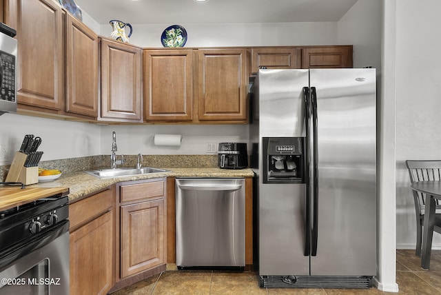 kitchen featuring brown cabinets, light tile patterned floors, appliances with stainless steel finishes, a sink, and light stone countertops