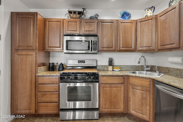 kitchen featuring appliances with stainless steel finishes, brown cabinetry, a sink, and light stone counters