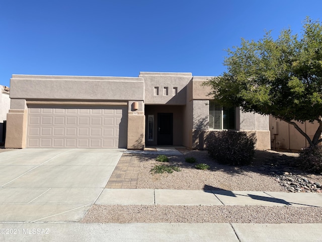 pueblo-style home with concrete driveway, stucco siding, and an attached garage