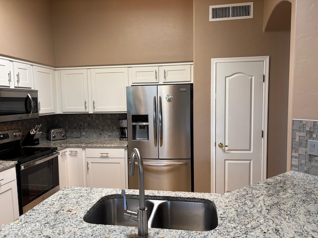kitchen with visible vents, decorative backsplash, white cabinetry, a sink, and stainless steel appliances