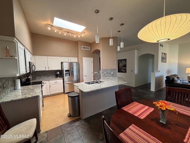 kitchen with stainless steel fridge, a sink, arched walkways, a peninsula, and visible vents