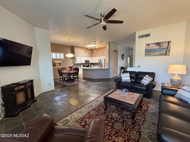 living room featuring visible vents, stone tile floors, a wood stove, baseboards, and a ceiling fan