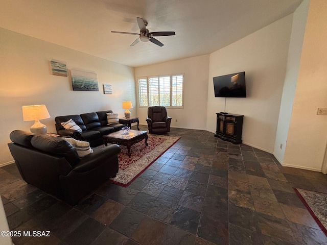 living area with baseboards, ceiling fan, a wood stove, and stone tile flooring