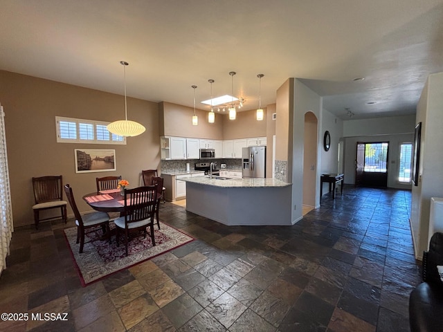 kitchen with stainless steel appliances, white cabinetry, a sink, and stone tile flooring