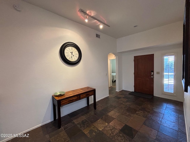 entrance foyer with stone tile floors, arched walkways, baseboards, and visible vents