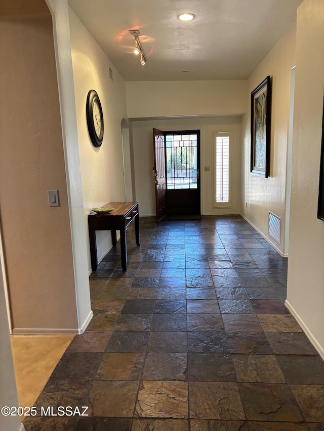 entryway featuring arched walkways, baseboards, visible vents, and stone tile flooring
