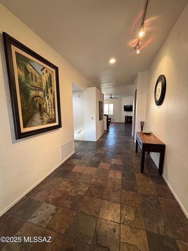corridor featuring stone tile flooring, baseboards, visible vents, and track lighting