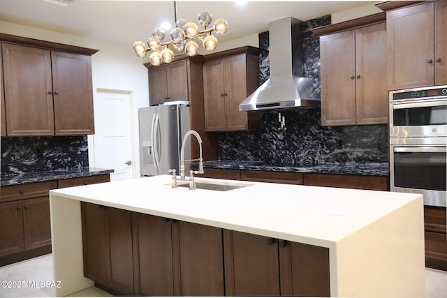 kitchen featuring range hood, a kitchen island with sink, tasteful backsplash, appliances with stainless steel finishes, and a sink