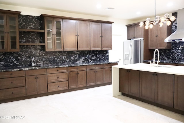 kitchen featuring tasteful backsplash, stainless steel refrigerator with ice dispenser, visible vents, glass insert cabinets, and wall chimney exhaust hood