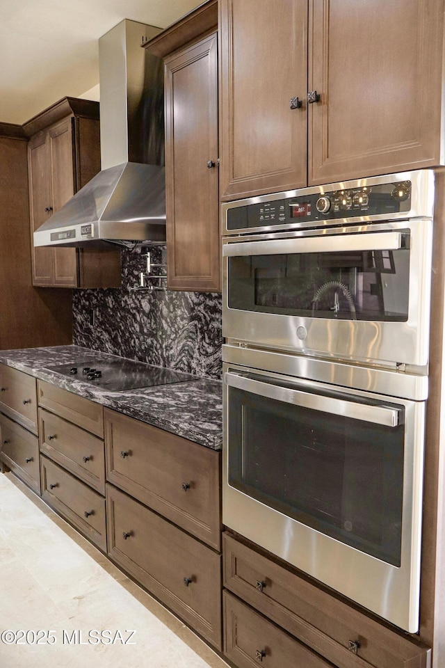 kitchen featuring black electric cooktop, stainless steel double oven, dark stone countertops, decorative backsplash, and wall chimney exhaust hood