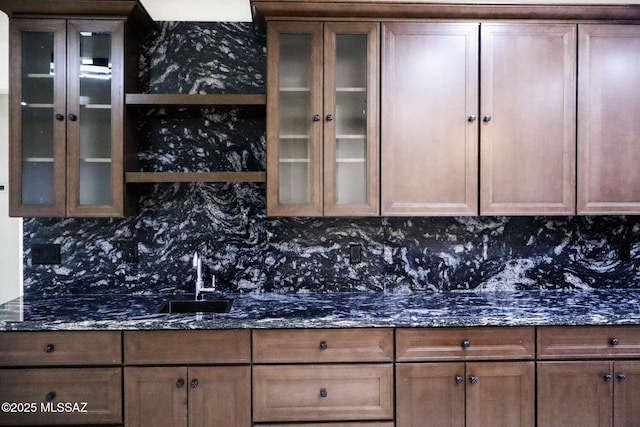 kitchen with glass insert cabinets, backsplash, a sink, and dark stone counters