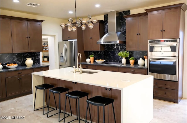 1077 Avenida Aire, Rio Rico, AZ 85648 - kitchen with stainless steel appliances, wall chimney exhaust hood, a sink, backsplash, and a breakfast bar