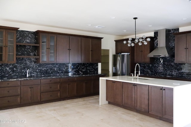 kitchen featuring wall chimney range hood, a sink, stainless steel refrigerator with ice dispenser, and glass insert cabinets