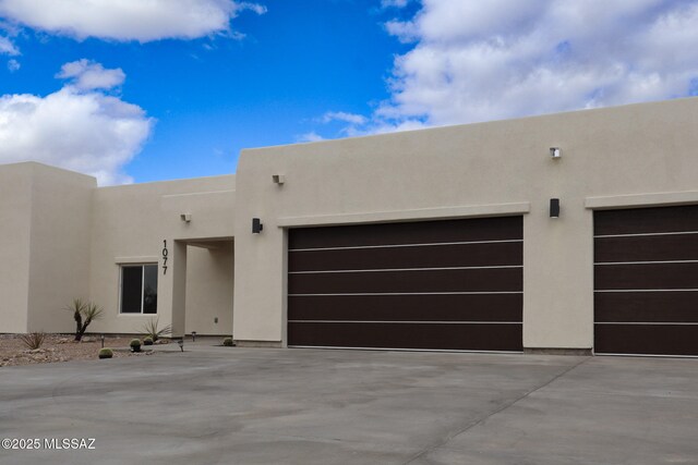 pueblo revival-style home with stucco siding, an attached garage, and driveway