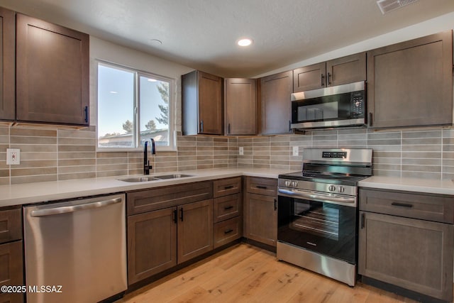 kitchen with light wood-type flooring, appliances with stainless steel finishes, light countertops, and a sink