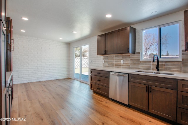 kitchen with light wood finished floors, light countertops, a sink, brick wall, and dishwasher