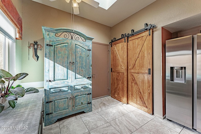 interior space featuring light tile patterned floors, a textured wall, a barn door, a skylight, and a ceiling fan