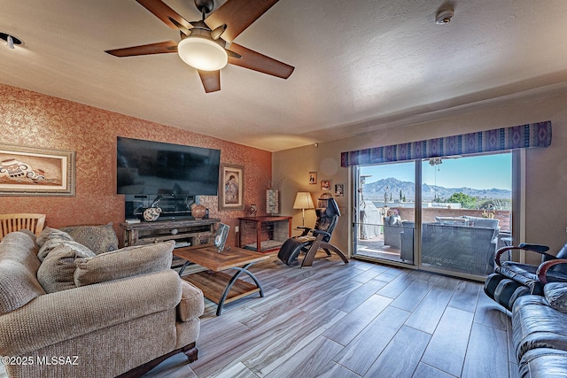 living room with wallpapered walls, a ceiling fan, lofted ceiling, wood finished floors, and a textured ceiling