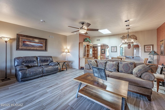 living area with ceiling fan with notable chandelier, arched walkways, visible vents, and wood finished floors