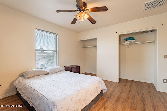 bedroom with ceiling fan, wood finished floors, visible vents, baseboards, and two closets