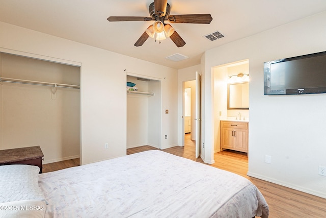 bedroom featuring visible vents, baseboards, ensuite bath, light wood-style floors, and two closets