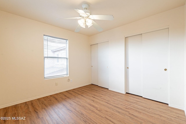 unfurnished bedroom featuring baseboards, ceiling fan, light wood finished floors, and multiple closets