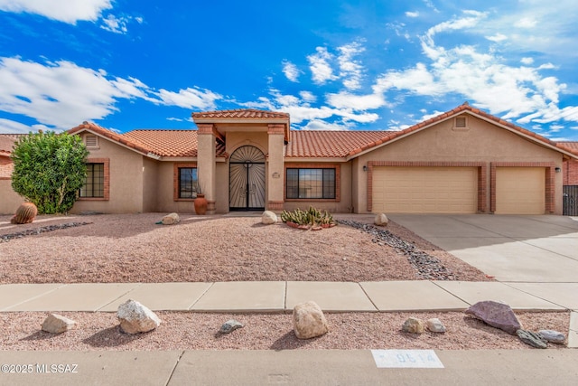 mediterranean / spanish-style home featuring a garage, a tiled roof, driveway, and stucco siding