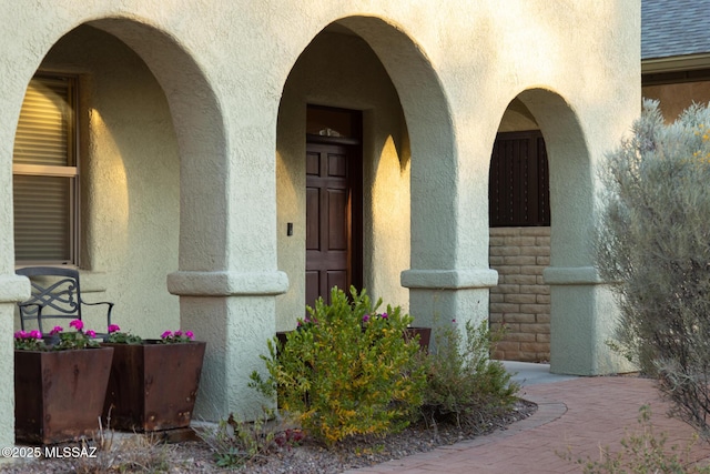 entrance to property featuring roof with shingles and stucco siding