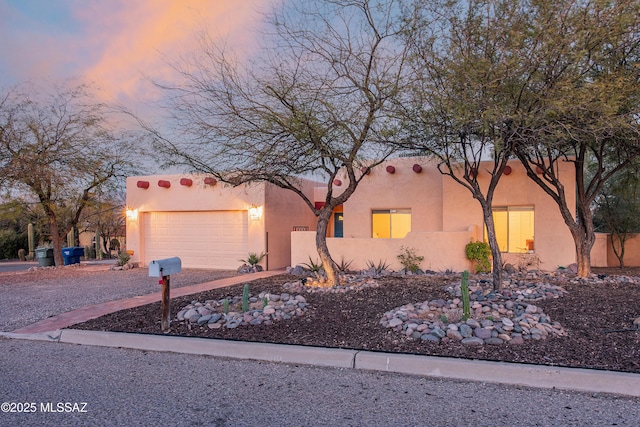 adobe home featuring an attached garage, driveway, and stucco siding