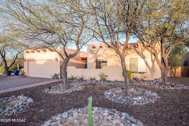 pueblo-style house with driveway, an attached garage, and stucco siding