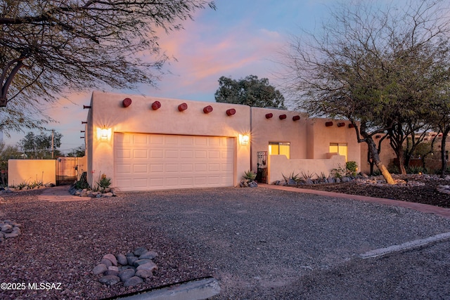 pueblo-style home with driveway, an attached garage, fence, and stucco siding