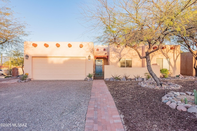 adobe home featuring a garage, gravel driveway, and stucco siding