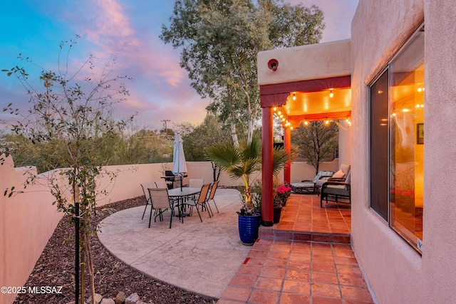 patio terrace at dusk featuring outdoor dining area and a fenced backyard