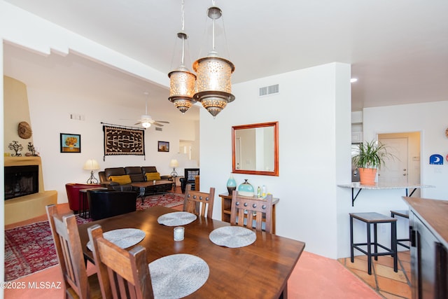 dining area featuring ceiling fan with notable chandelier, a fireplace, and visible vents