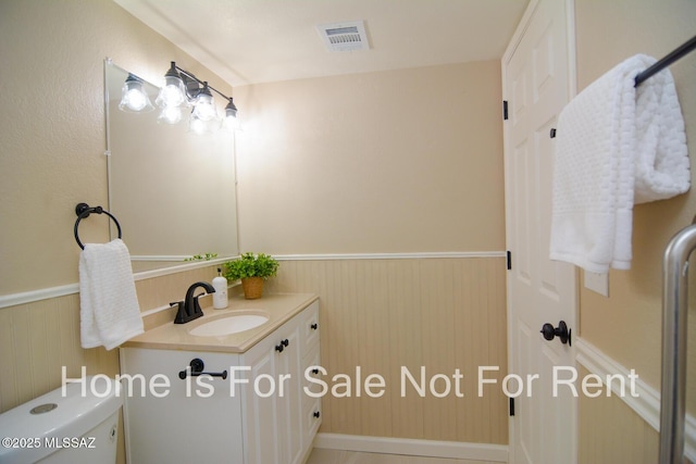 half bath with a wainscoted wall, toilet, vanity, and visible vents