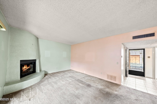 unfurnished living room with a large fireplace, carpet floors, a textured ceiling, and visible vents